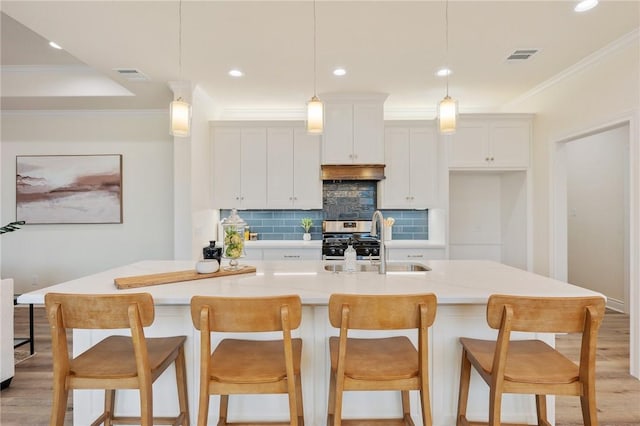 kitchen featuring white cabinets, a kitchen island with sink, and ornamental molding