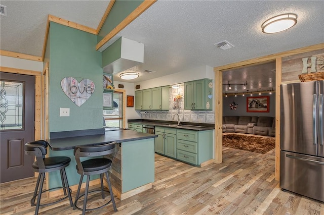 kitchen with appliances with stainless steel finishes, a breakfast bar, wood-type flooring, sink, and green cabinetry