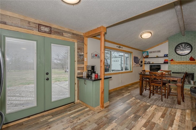 dining area with french doors, wood-type flooring, lofted ceiling with beams, a textured ceiling, and a fireplace