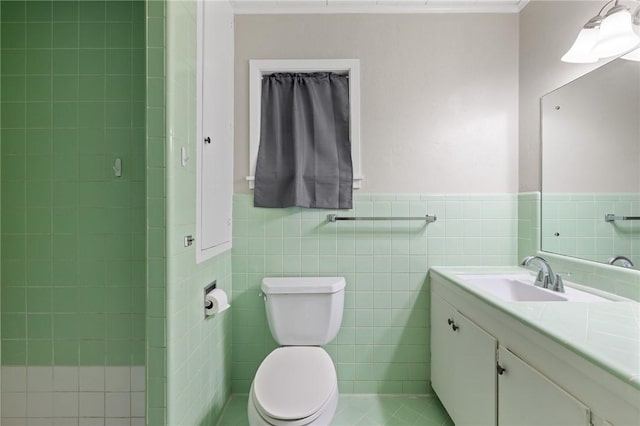 full bathroom with a tile shower, vanity, a wainscoted wall, toilet, and tile walls