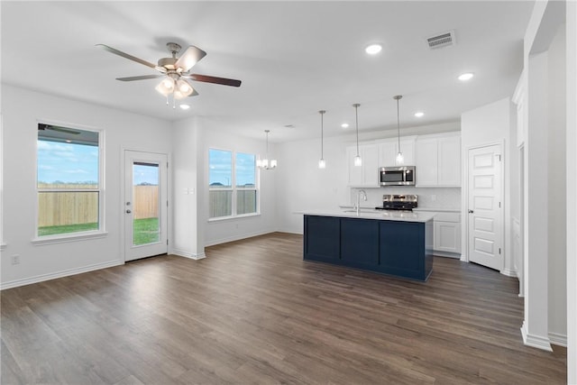 kitchen featuring pendant lighting, appliances with stainless steel finishes, white cabinetry, ceiling fan with notable chandelier, and an island with sink