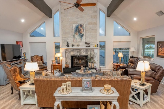 living room with beamed ceiling, a stone fireplace, high vaulted ceiling, and light hardwood / wood-style flooring