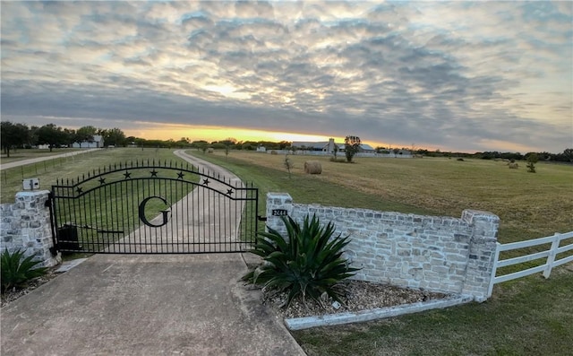 gate at dusk featuring a lawn and a rural view