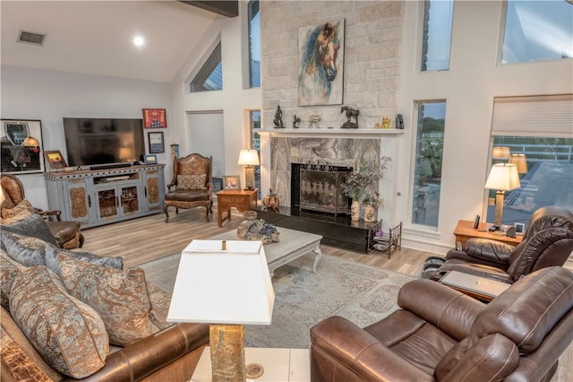 living room featuring beam ceiling, a fireplace, high vaulted ceiling, and light hardwood / wood-style floors