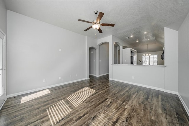 unfurnished living room with dark wood-type flooring, baseboards, ceiling fan with notable chandelier, arched walkways, and a textured ceiling