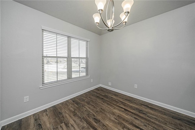 spare room featuring a chandelier, dark wood finished floors, and baseboards