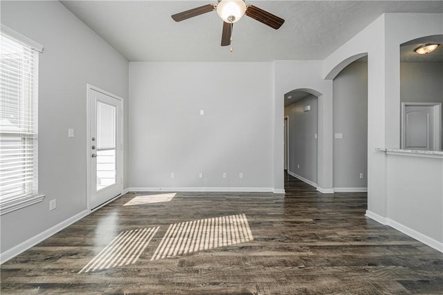 empty room featuring baseboards, arched walkways, dark wood-type flooring, and a ceiling fan