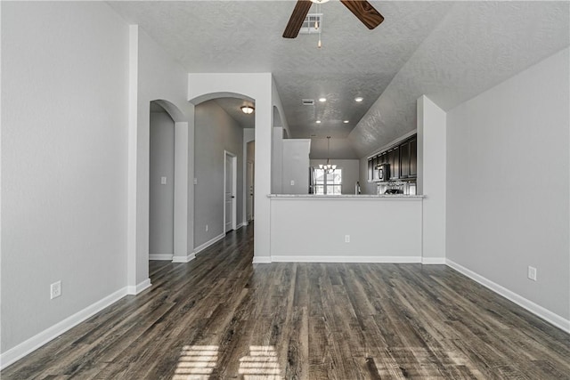 unfurnished living room with ceiling fan with notable chandelier, dark wood-style flooring, and baseboards