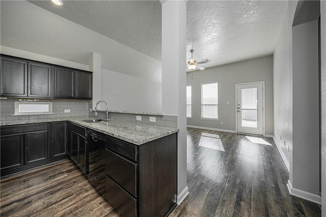 kitchen featuring dark wood-type flooring, a ceiling fan, a sink, light stone counters, and decorative backsplash