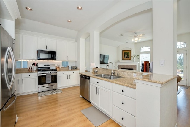 kitchen with sink, appliances with stainless steel finishes, white cabinetry, light stone countertops, and light wood-type flooring