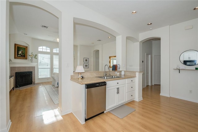 kitchen with sink, dishwasher, white cabinetry, light hardwood / wood-style floors, and a tiled fireplace