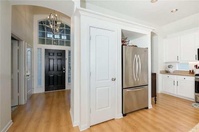 kitchen featuring decorative light fixtures, light hardwood / wood-style flooring, appliances with stainless steel finishes, a towering ceiling, and white cabinets