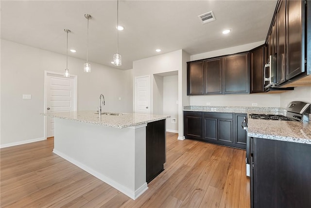 kitchen with a kitchen island with sink, sink, hanging light fixtures, and light wood-type flooring