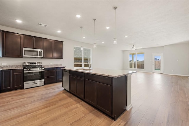 kitchen featuring a center island with sink, sink, hanging light fixtures, light hardwood / wood-style flooring, and stainless steel appliances