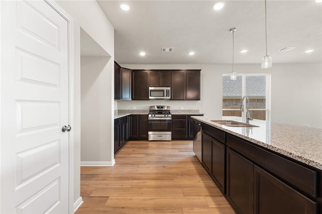 kitchen with dark brown cabinetry, stainless steel appliances, sink, light hardwood / wood-style floors, and hanging light fixtures