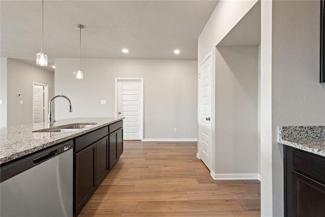 kitchen featuring light stone countertops, sink, stainless steel dishwasher, pendant lighting, and light hardwood / wood-style floors