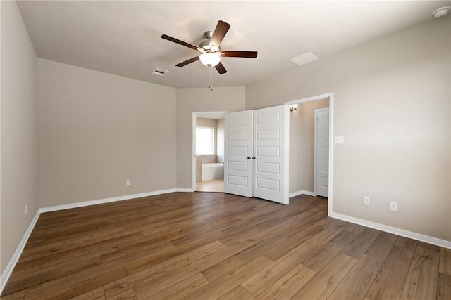 unfurnished bedroom with ceiling fan, ensuite bathroom, and hardwood / wood-style flooring