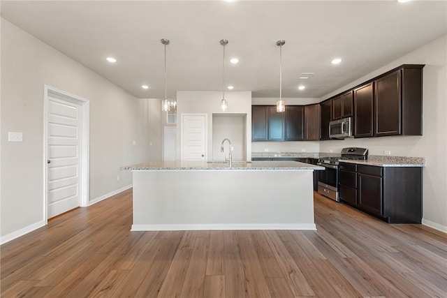 kitchen with a center island with sink, light hardwood / wood-style flooring, light stone countertops, appliances with stainless steel finishes, and dark brown cabinetry