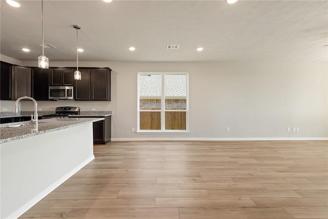 kitchen with light stone countertops, sink, light hardwood / wood-style flooring, dark brown cabinets, and appliances with stainless steel finishes