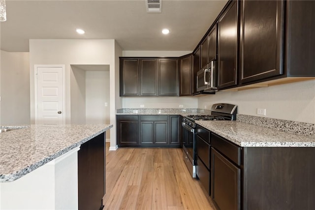 kitchen featuring dark brown cabinets, light stone countertops, light wood-type flooring, and appliances with stainless steel finishes