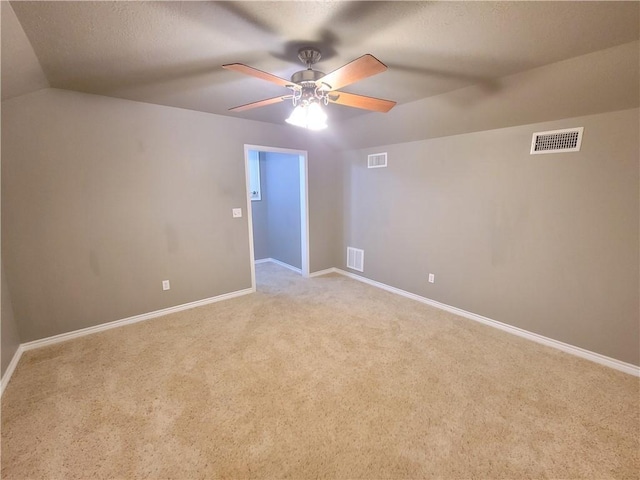 empty room featuring a textured ceiling, light colored carpet, vaulted ceiling, and ceiling fan