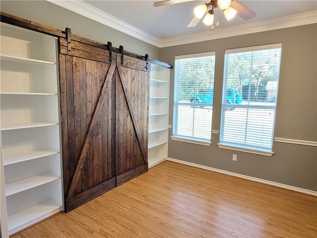 interior space with hardwood / wood-style flooring, ceiling fan, a barn door, and crown molding