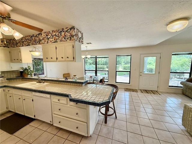 28 Sammy Snead Dr, Hilltop Lakes, TX 77871 - kitchen featuring white dishwasher, a sink, a peninsula, tile countertops, and light tile patterned floors