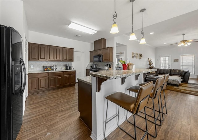 kitchen with black appliances, a breakfast bar area, dark wood finished floors, and decorative backsplash