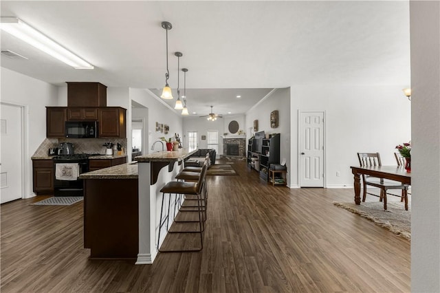 kitchen with dark wood-style flooring, gas stove, open floor plan, black microwave, and a kitchen breakfast bar