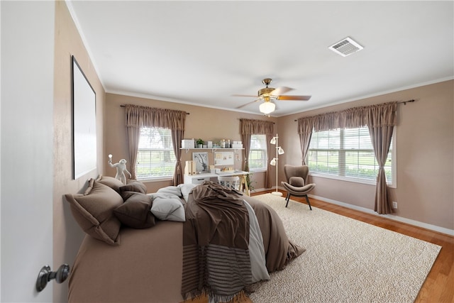 bedroom featuring wood-type flooring, multiple windows, crown molding, and ceiling fan