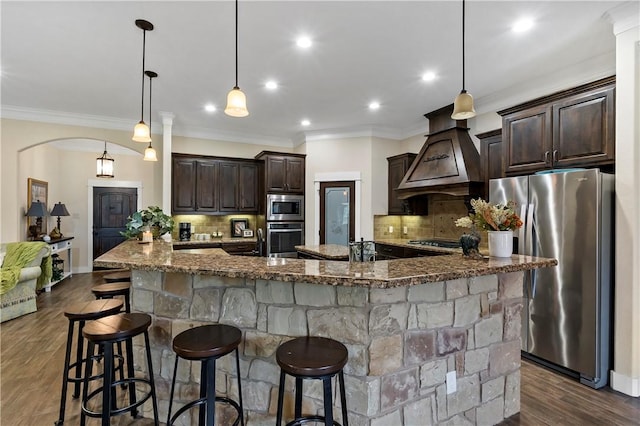 kitchen with dark brown cabinets, appliances with stainless steel finishes, a breakfast bar area, dark stone countertops, and backsplash