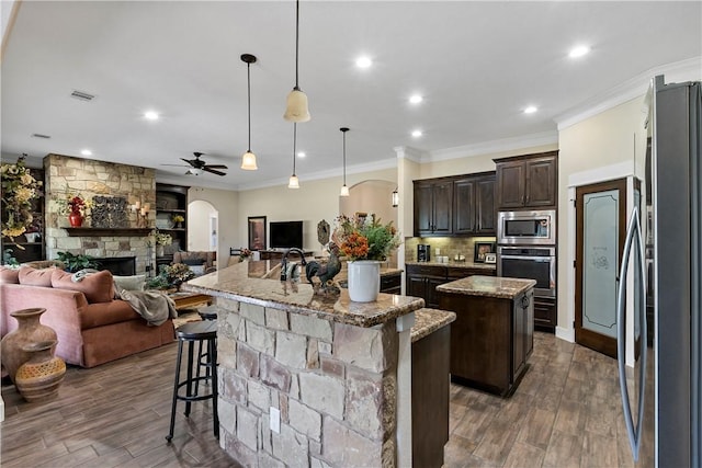 kitchen with stainless steel appliances, dark brown cabinetry, a center island with sink, and open floor plan