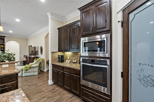 kitchen with dark brown cabinetry, tasteful backsplash, light stone counters, arched walkways, and stainless steel appliances