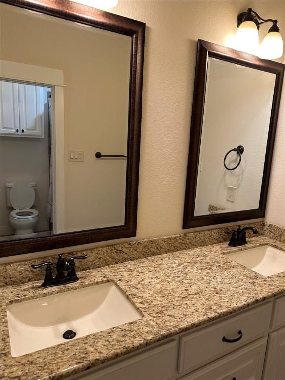 bathroom with double vanity, toilet, and a sink