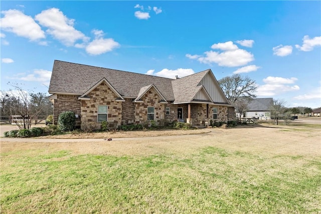 view of front of property with stone siding, a front yard, and roof with shingles