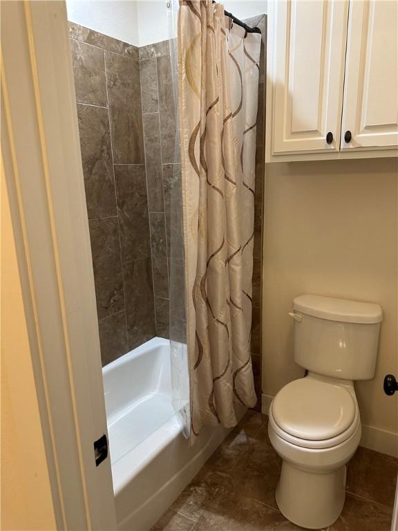 bathroom with baseboards, shower / bath combo with shower curtain, and toilet