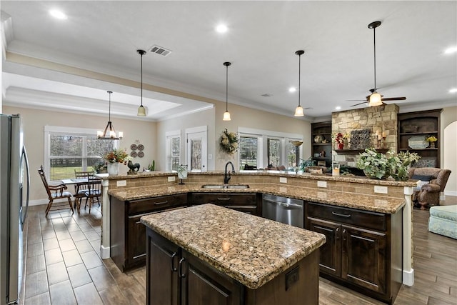 kitchen with visible vents, appliances with stainless steel finishes, a sink, ceiling fan with notable chandelier, and an island with sink