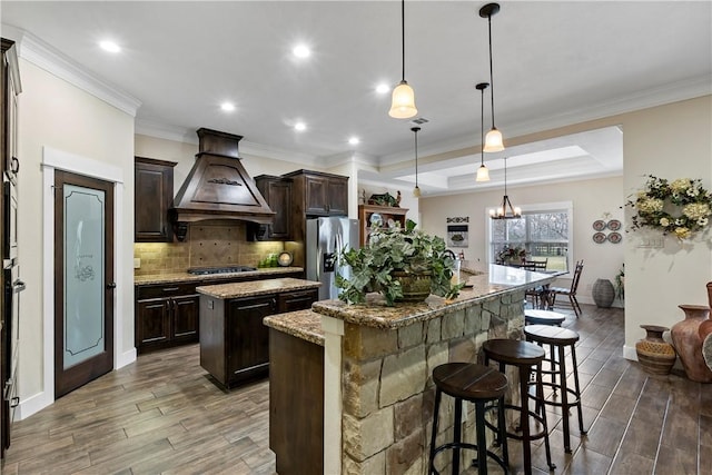 kitchen featuring dark brown cabinets, a kitchen island with sink, wood finished floors, custom range hood, and stainless steel refrigerator with ice dispenser