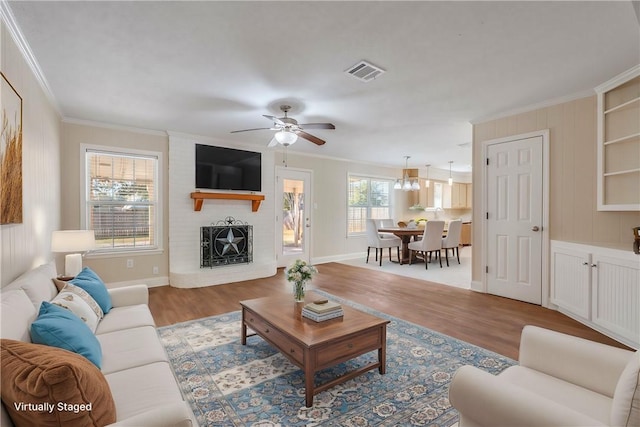 living room featuring a fireplace, crown molding, ceiling fan with notable chandelier, and light hardwood / wood-style floors