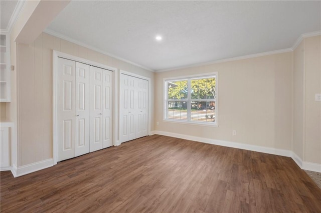 unfurnished bedroom with dark hardwood / wood-style floors, crown molding, and multiple closets