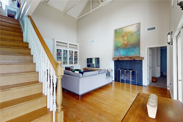 living room with a fireplace, high vaulted ceiling, beam ceiling, and hardwood / wood-style flooring