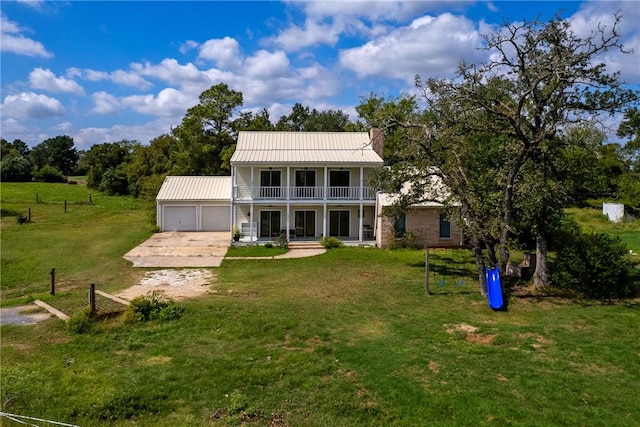 rear view of property featuring a garage, a yard, covered porch, and a balcony