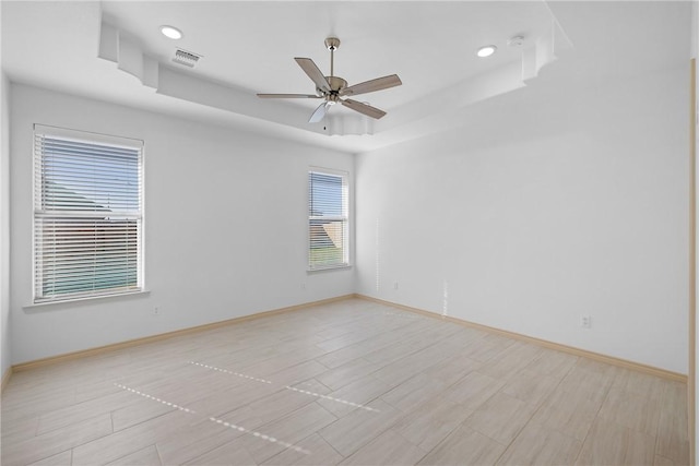 spare room featuring a tray ceiling, ceiling fan, and light wood-type flooring