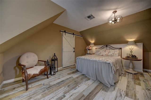 bedroom with a barn door, lofted ceiling, and light wood-type flooring