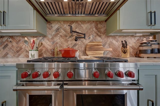 kitchen featuring wall chimney exhaust hood, decorative backsplash, range with two ovens, and light stone countertops