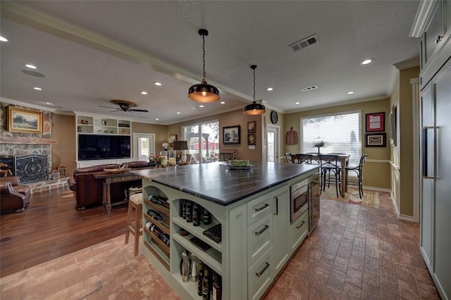 kitchen featuring a center island, hanging light fixtures, built in appliances, crown molding, and a fireplace