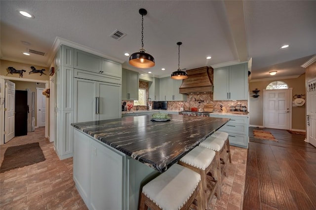 kitchen with backsplash, premium range hood, dark stone counters, crown molding, and a kitchen island