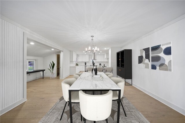 dining area with light wood-type flooring, vaulted ceiling, crown molding, and a notable chandelier