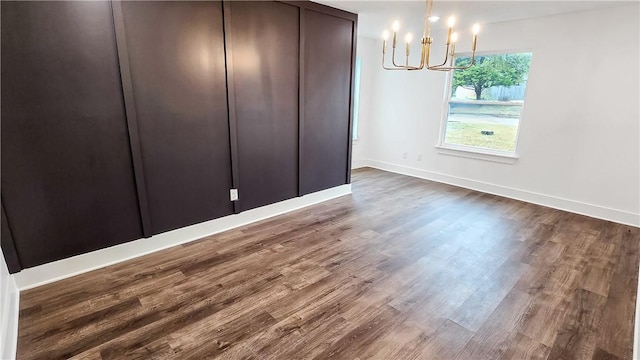 unfurnished dining area featuring baseboards, an inviting chandelier, and dark wood-style flooring