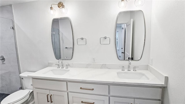 full bathroom featuring double vanity, toilet, a tile shower, and a sink